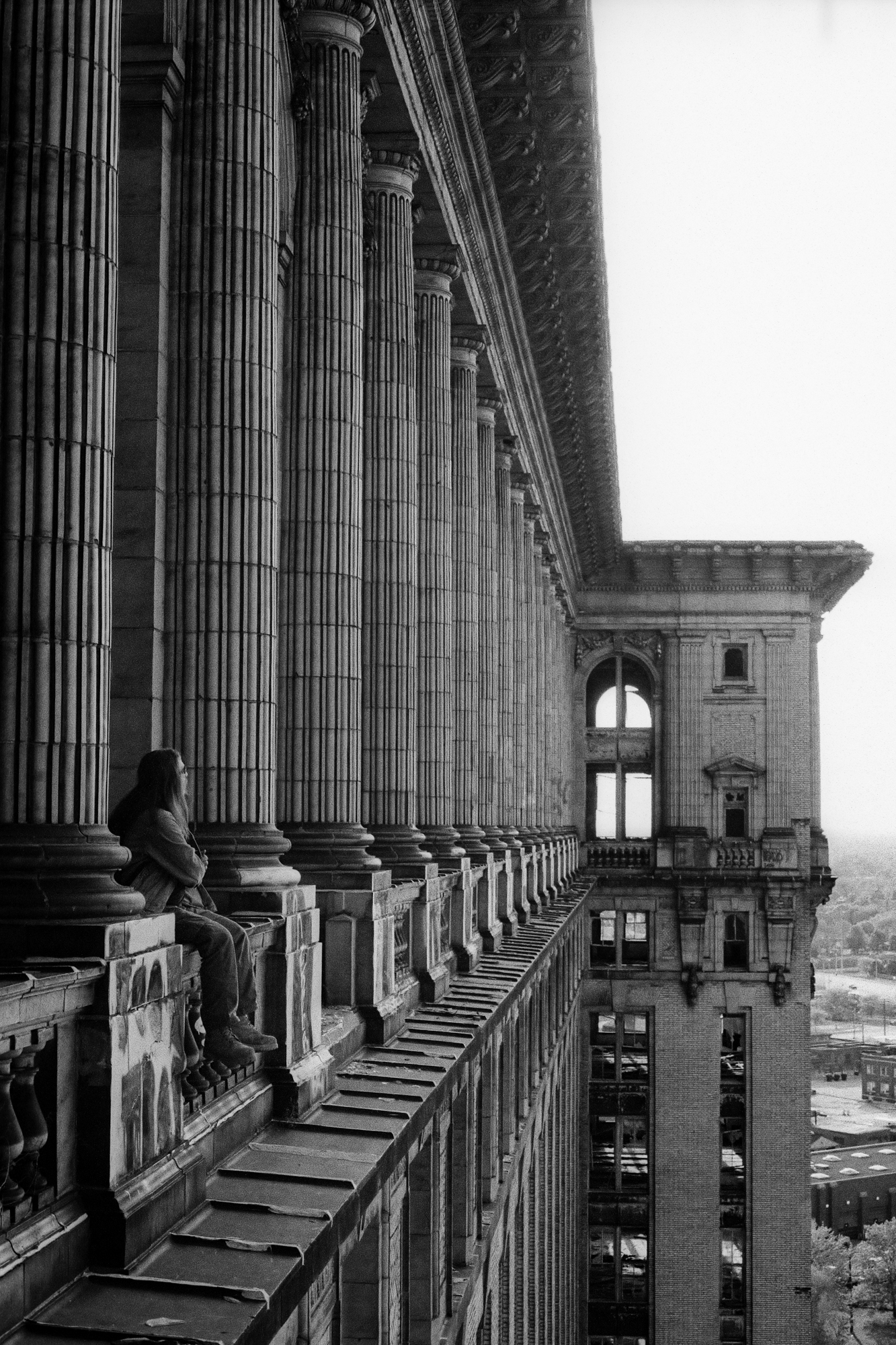Elevated view of the exterior of Michigan Central Station with a figure sitting on a railing in Detroit, MI.